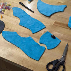 A photograph of bright blue cut fabric pattern pieces laid out on a table.