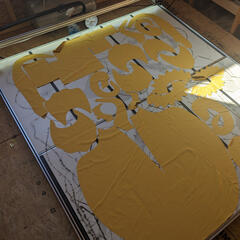 A photograph of a laser cutter cutting a sheet of gold fabric; some of the off-cuts have been removed, leaving the cut pattern pieces behind.