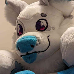 A close photograph of the smiling face of a plush dog with gray spots and a blue nose.