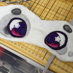 A photograph of a pair of embroidered eyes stitched onto a long white band of fabric.
