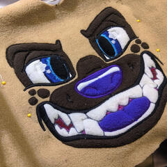 A close photograph showing the machine embroidered face of a stylized hyena.