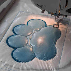 A photograph of an embroidery machine stitching out a design of a pawpad.