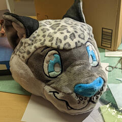 A photograph of the head of a plush snow leopard, showing the embroidered eyes, mouth, and nose.