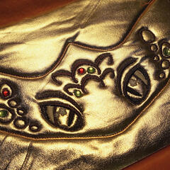 A photograph showing a pair of machine embroidered eyes and scales on a band of gold fabric.